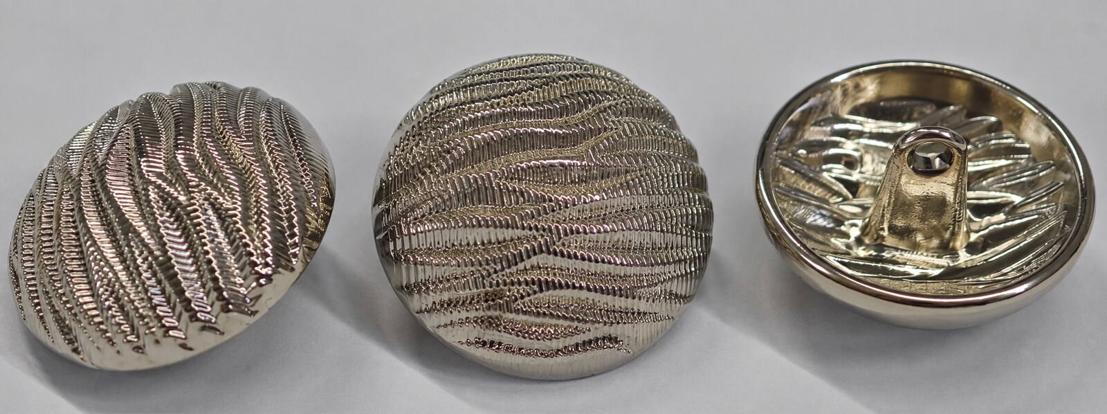 Round silver-tone garment button with a flowing wave texture