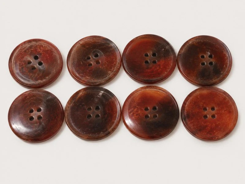 KN2408001 narrow-rim brown horn buttons with four sewing holes.