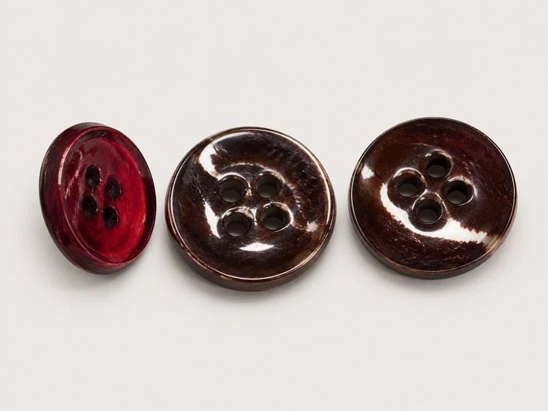 Burgundy-dyed four-hole shell button shown at three angles.