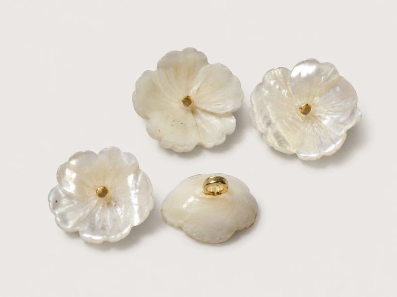 Flower-shaped shell button with gold-tone center and shank details.
